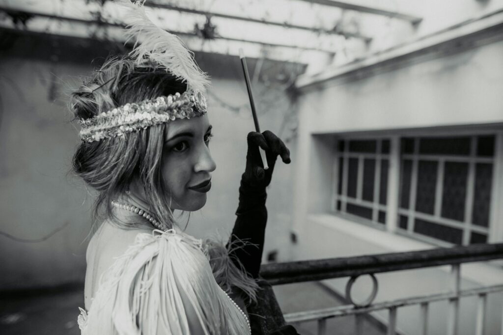 Black and white photo of a woman in vintage attire with feathered headband on a balcony.